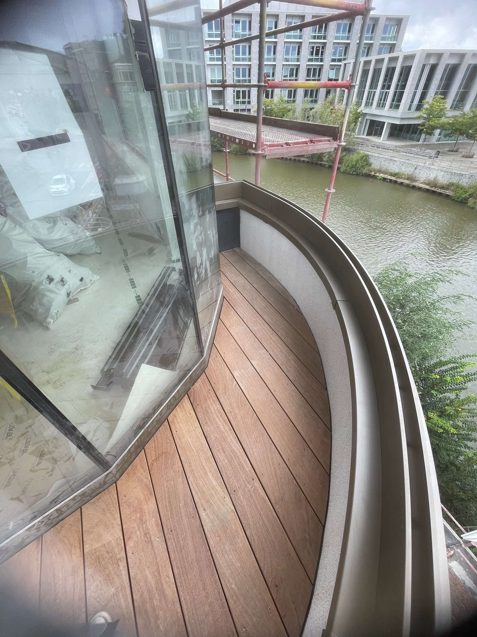 Smal gebogen hardhouten dakterras langs een glazen gevel aan de Leie in Deinze