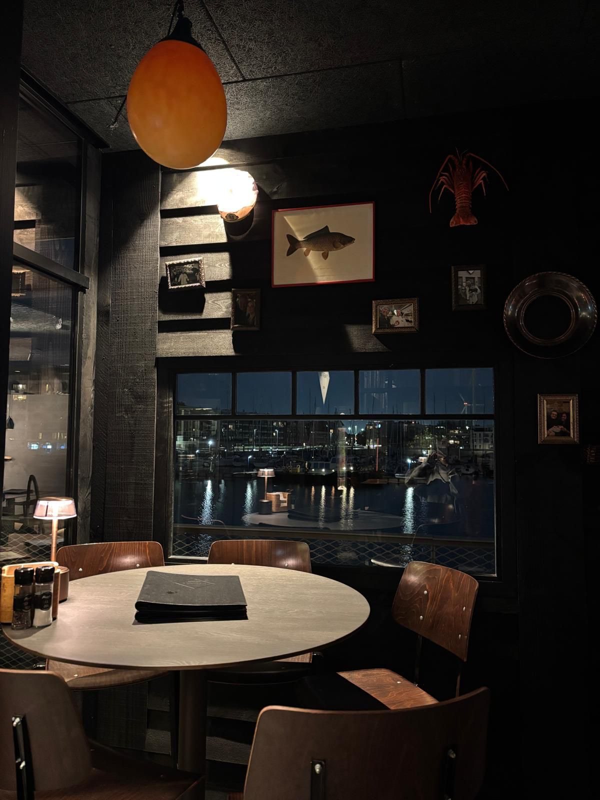 Zwarte houten wanden rond een groot raam met zicht op de jachthaven in restaurant 't Werftje, 's avonds